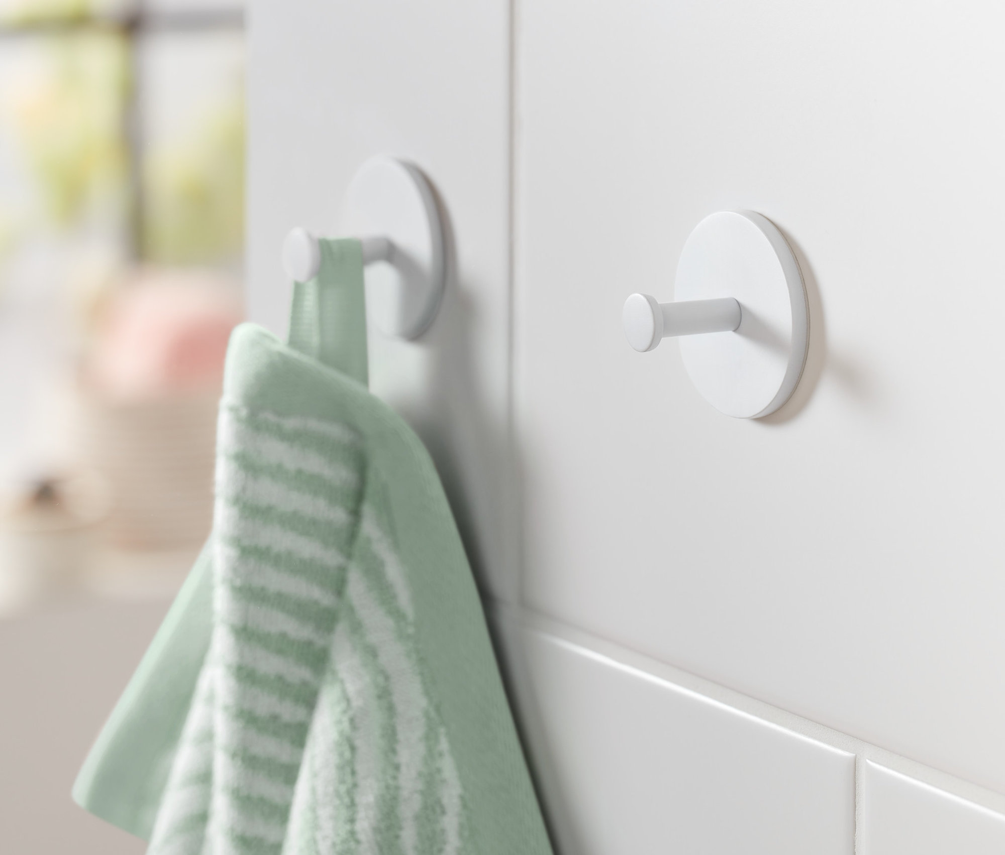 Beyaz bir duvara tutturulmuş iki beyaz kancadan birinde yeşil bir havlu asılı duruyor.