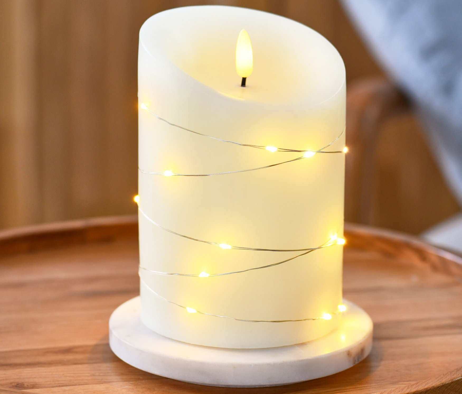 Yuvarlak ahşap bir masanın üzerinde mikro LED ışık zincirli gerçek balmumu LED mum duruyor.