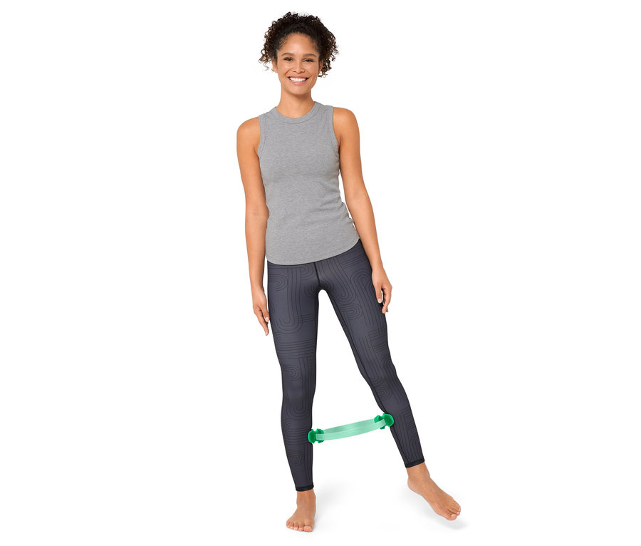 Kadın bacaklarının arasında bir pilates halkasıyla egzersiz yapıyor.