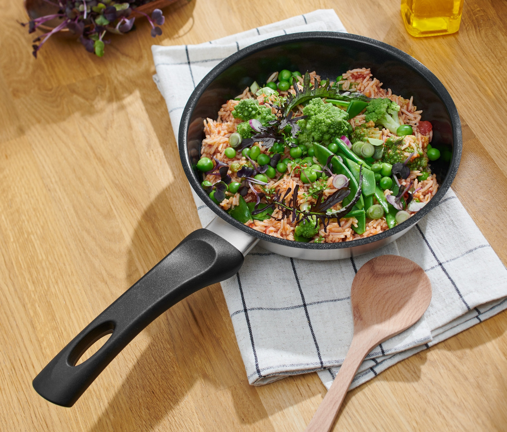 Seramik kaplamalı paslanmaz çelik tava, çapı yaklaşık 20 cm, kareli bir bez üzerinde yemekle birlikte.