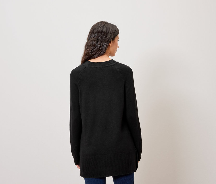 Siyah kazak ve mavi kot pantolon giyen, koyu renk dalgalı saçlı bir kadının arkadan görünümü.