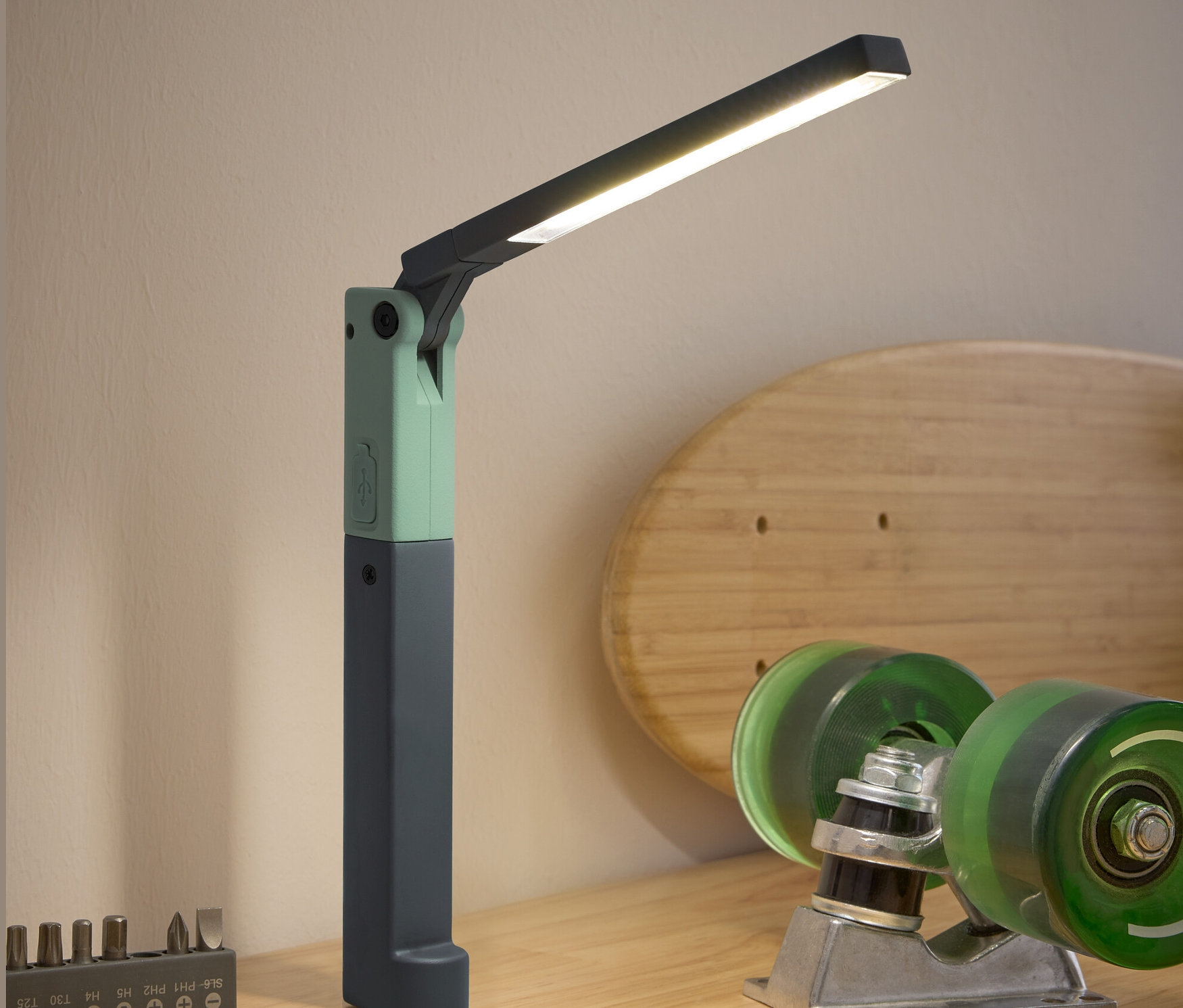 Ahşap bir masa üzerinde bir LED çalışma lambası, bir tornavida, bir bit seti ve kaykay aksesuarları bulunmaktadır.