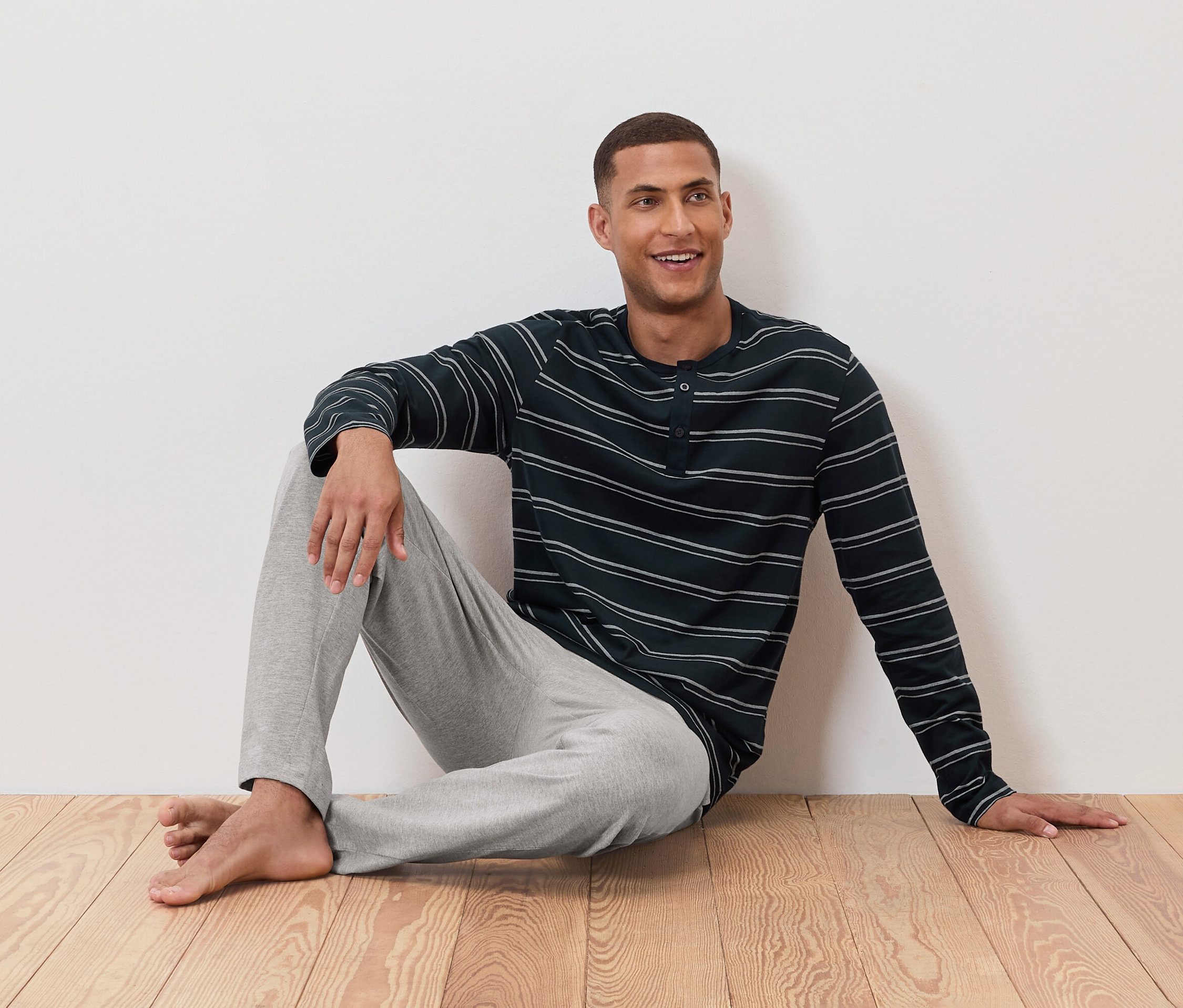 Adam yerde çizgili pijaması ve gri pantolonuyla oturuyor.