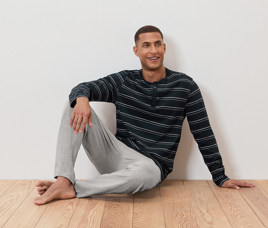 Adam yerde çizgili pijaması ve gri pantolonuyla oturuyor.