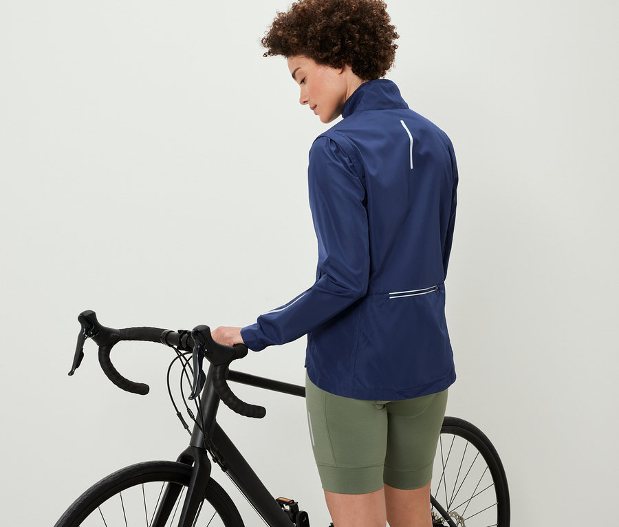 Kadın bisikletin yanında duruyor ve 2'si 1 arada bisiklet montu giyiyor.