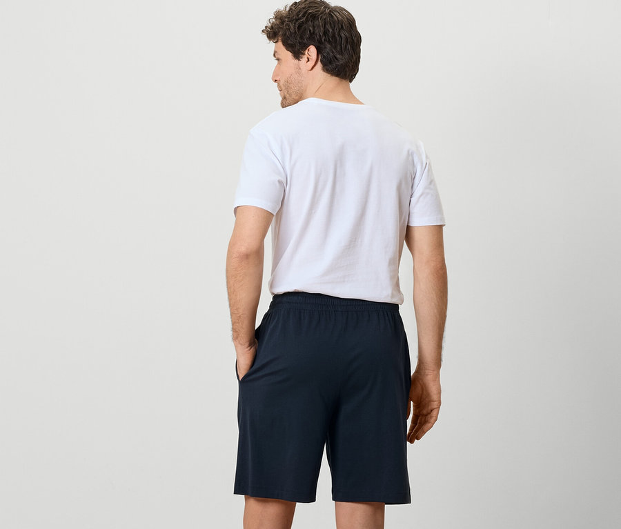 Arkası dönük bir adam üzerinde 2 adet pijama şortu ve tişört var.