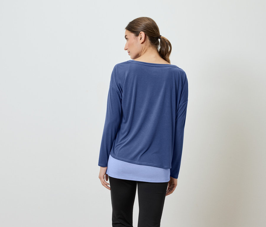 Sırtı kameraya dönük bir kadın, mavi uzun kollu bir gömlek ve siyah pantolon giyiyor.