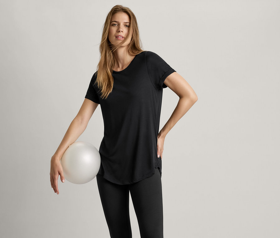 Kadın bir top tutuyor ve siyah uzun bir tişört giyiyor.