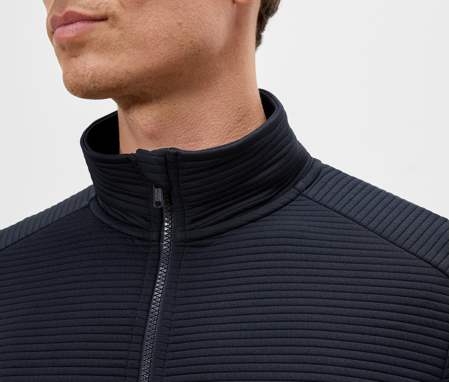 Yakası dik, lacivert, fermuarlı bir ceket giyen bir adamın yakın çekimi.