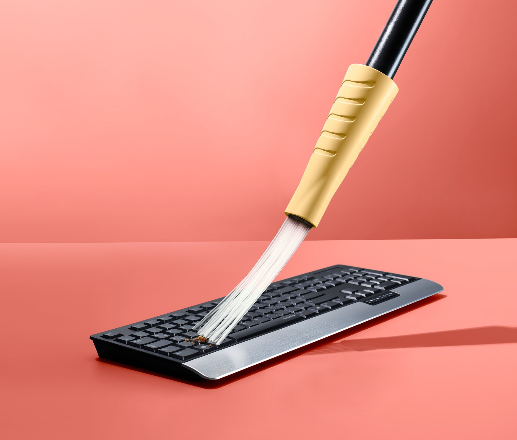 Elektrikli süpürge başlığı pembe bir arka plan üzerinde klavyeyi temizliyor.