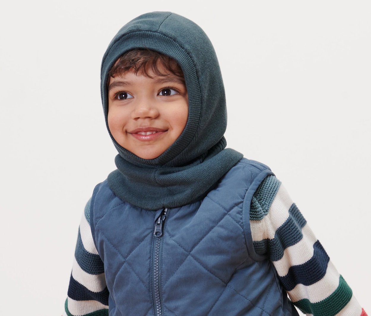 Gülümseyen çocuk, Küçük Çocuk Kar Maskesi, kapitone yelek ve çizgili kazak giyiyor.