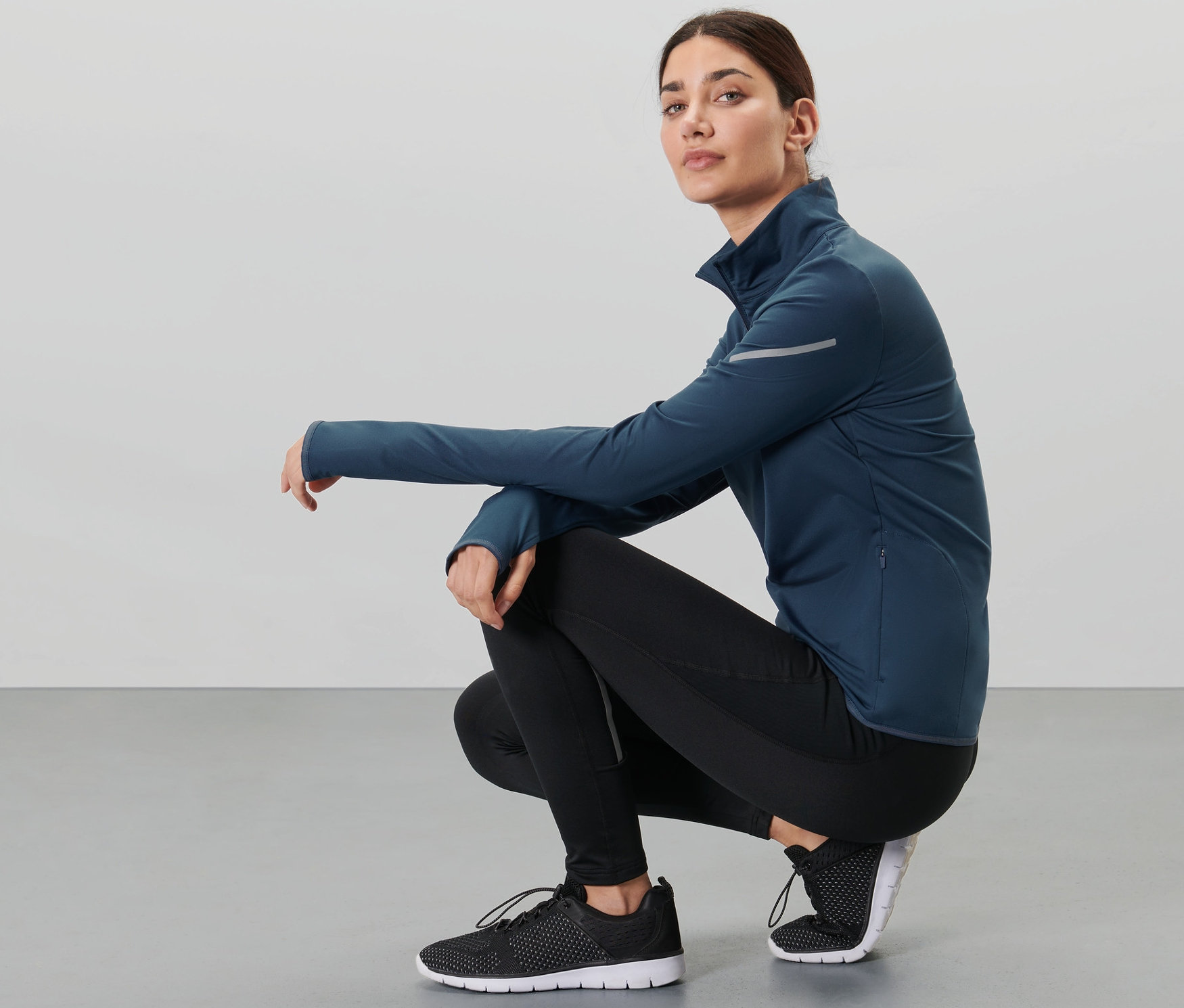 Çömelmiş bir kadın, koyu mavi fonksiyonel termal üst giyiyor.
