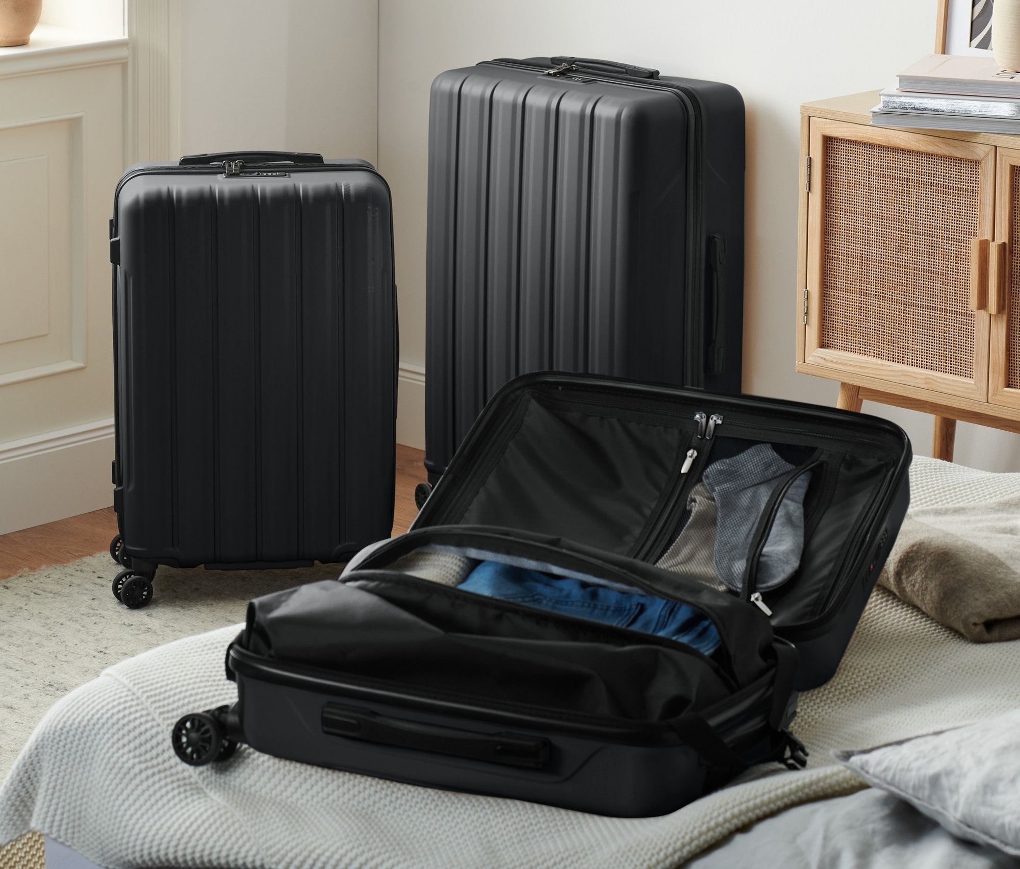 Üç siyah sert bavul, biri yatak üzerinde açık halde.