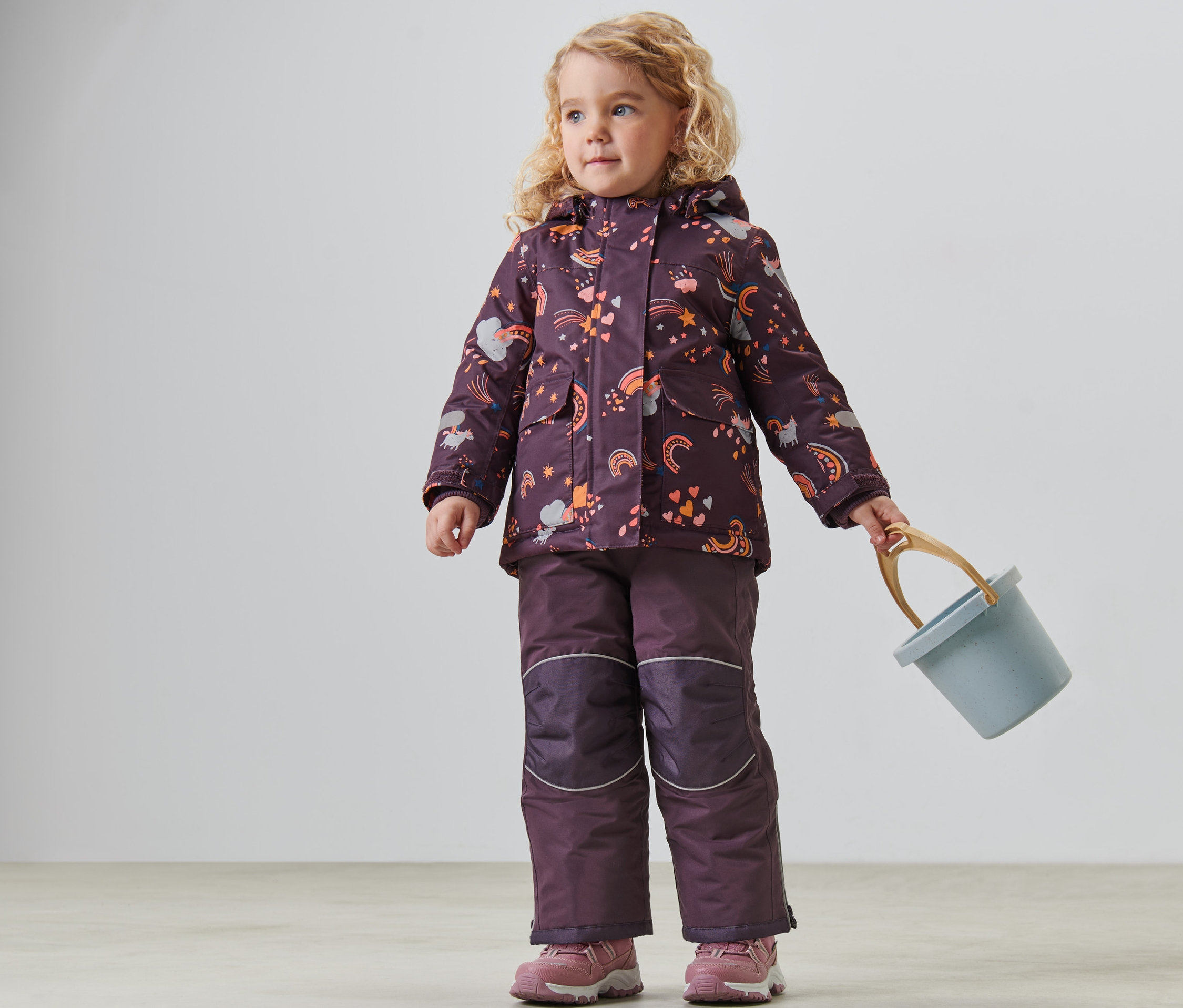 Çocuk kar takımını giyen kız çocuğu mavi bir kova tutuyor.