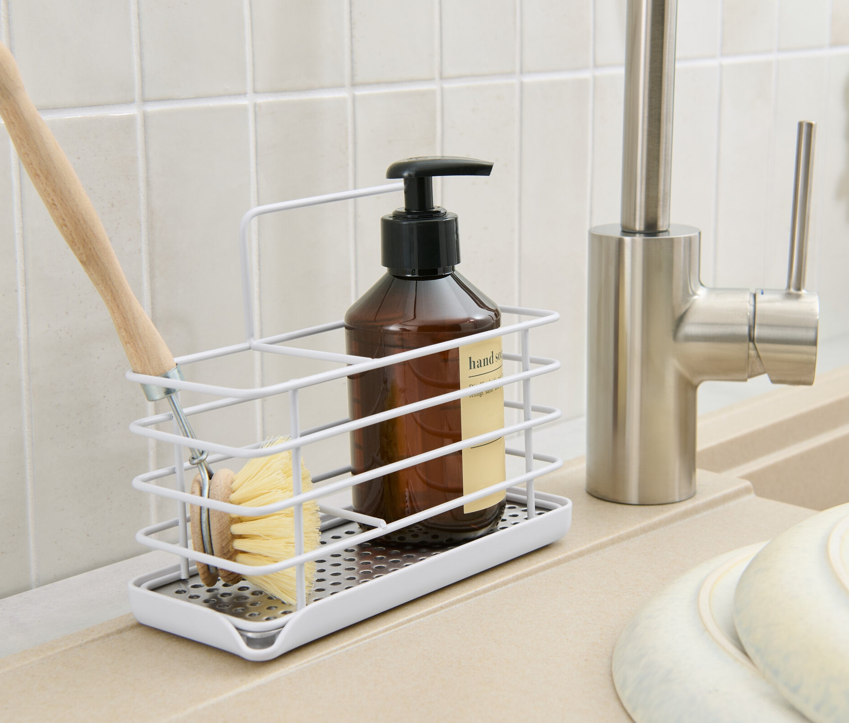 Mutfakta fırça, şişe ve sabunluk içeren metal bulaşık malzemesi standı bulunmaktadır.