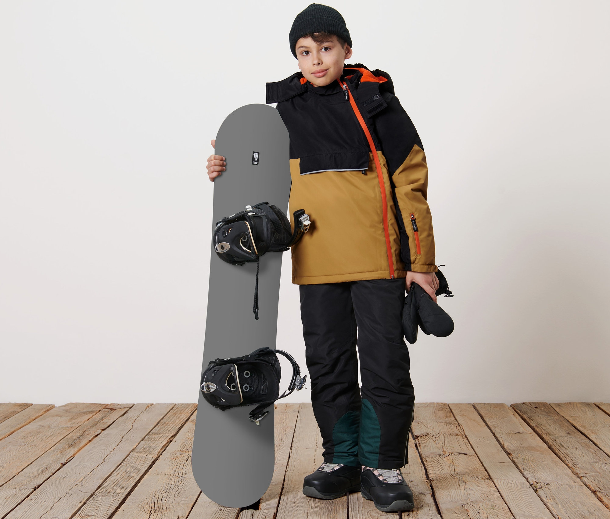 Çocuk bir snowboard tutuyor ve Çocuk Snowboard Montu giyiyor.