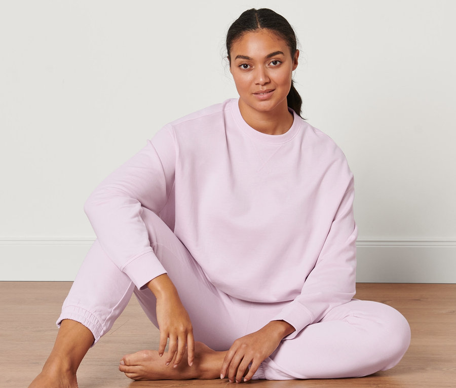 Kadın yerde oturuyor ve açık pembe, oversize yoga sweatshirt giyiyor.