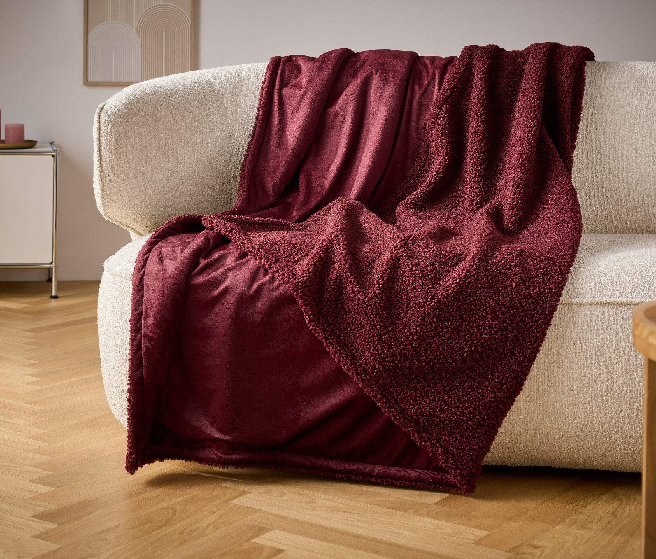 Krem rengi bir kanepenin üzerinde bordo bir battaniye duruyor