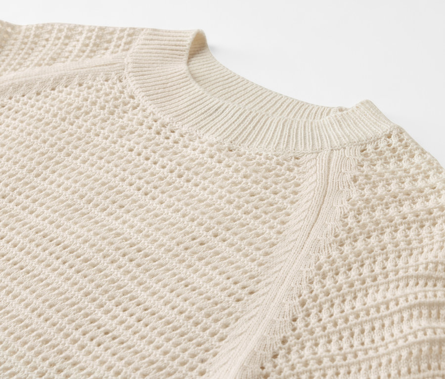 Beyaz bir arka plan üzerinde pointelle örgü bir kazak detayı.