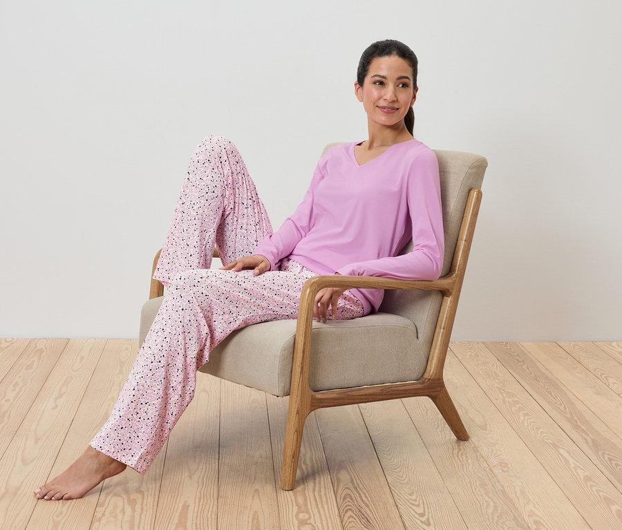 Kadın koltukta oturuyor ve baskılı mor bir pijama giyiyor.