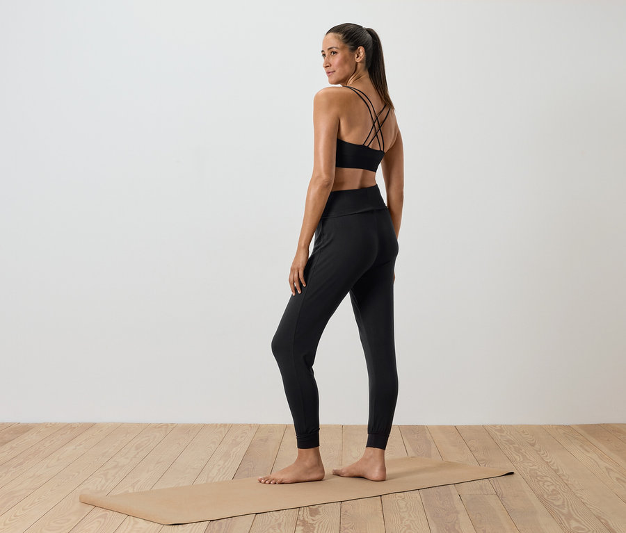 Siyah spor giyiminde bir kadın yoga matının üzerinde duruyor.