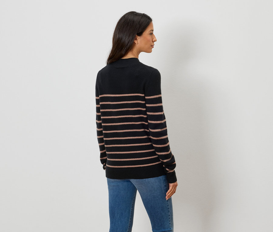 Omuz hizasında koyu renk saçlı bir kadının, yatay kahverengi çizgili siyah balıkçı yaka bir kazak ve mavi kot pantolon giydiği arka görünümü.