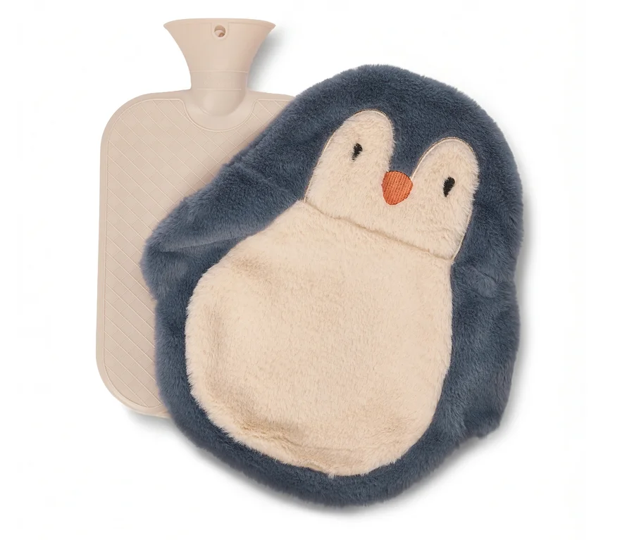 Bej renkli sıcak su torbası, krem karınlı ve turuncu gagalı, mavimsi gri penguen şeklinde peluş kılıfıyla birlikte duruyor.