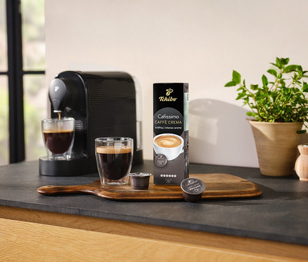 Kahve makinesi, bir bardak kahveyi Cafissimo Caffè Crema – 10 kapsül paketinin yanına hazırlıyor.
