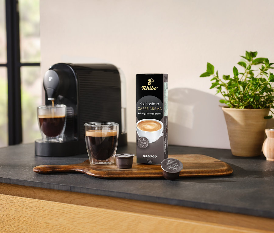 Kahve makinesi, bir bardak kahveyi Cafissimo Caffè Crema – 10 kapsül paketinin yanına hazırlıyor.