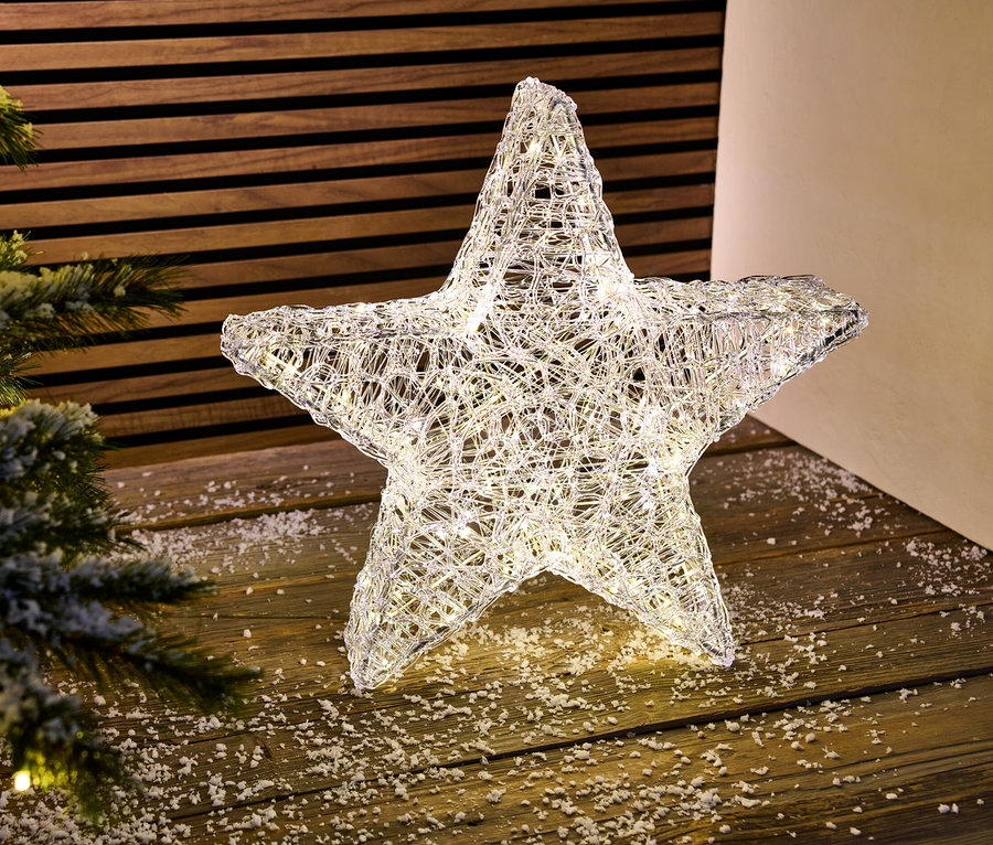 Işıklı bir LED dış mekan dekoratif yıldızı, bir Noel ağacının yanında ahşap bir zeminde duruyor.