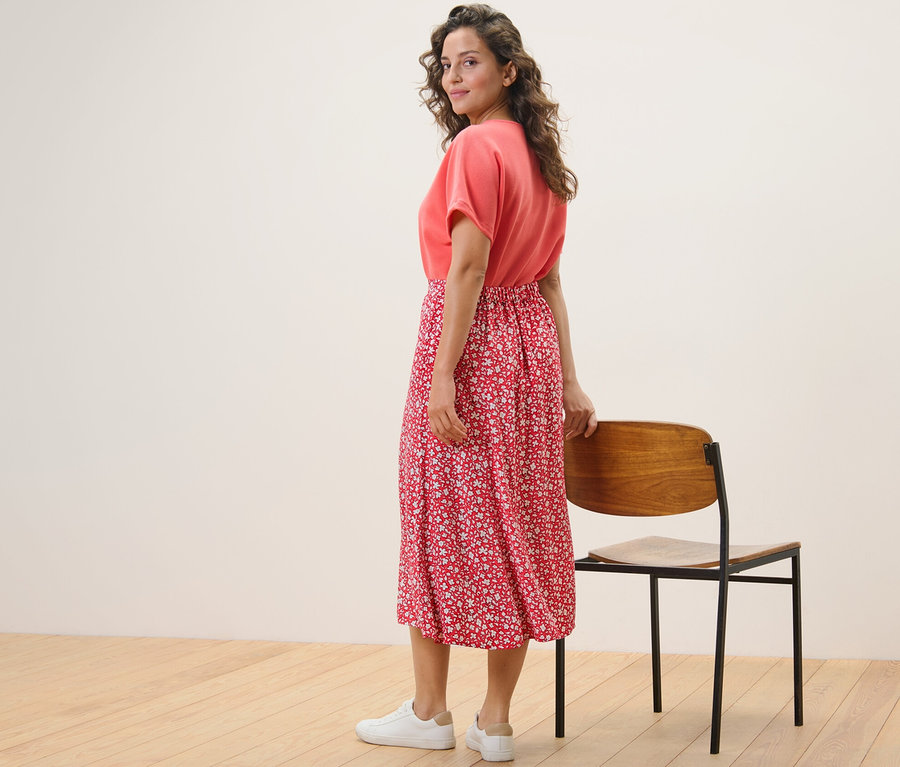 Omuz üzerinden bakan bir kadın, kırmızı baskılı midi etekle poz veriyor.