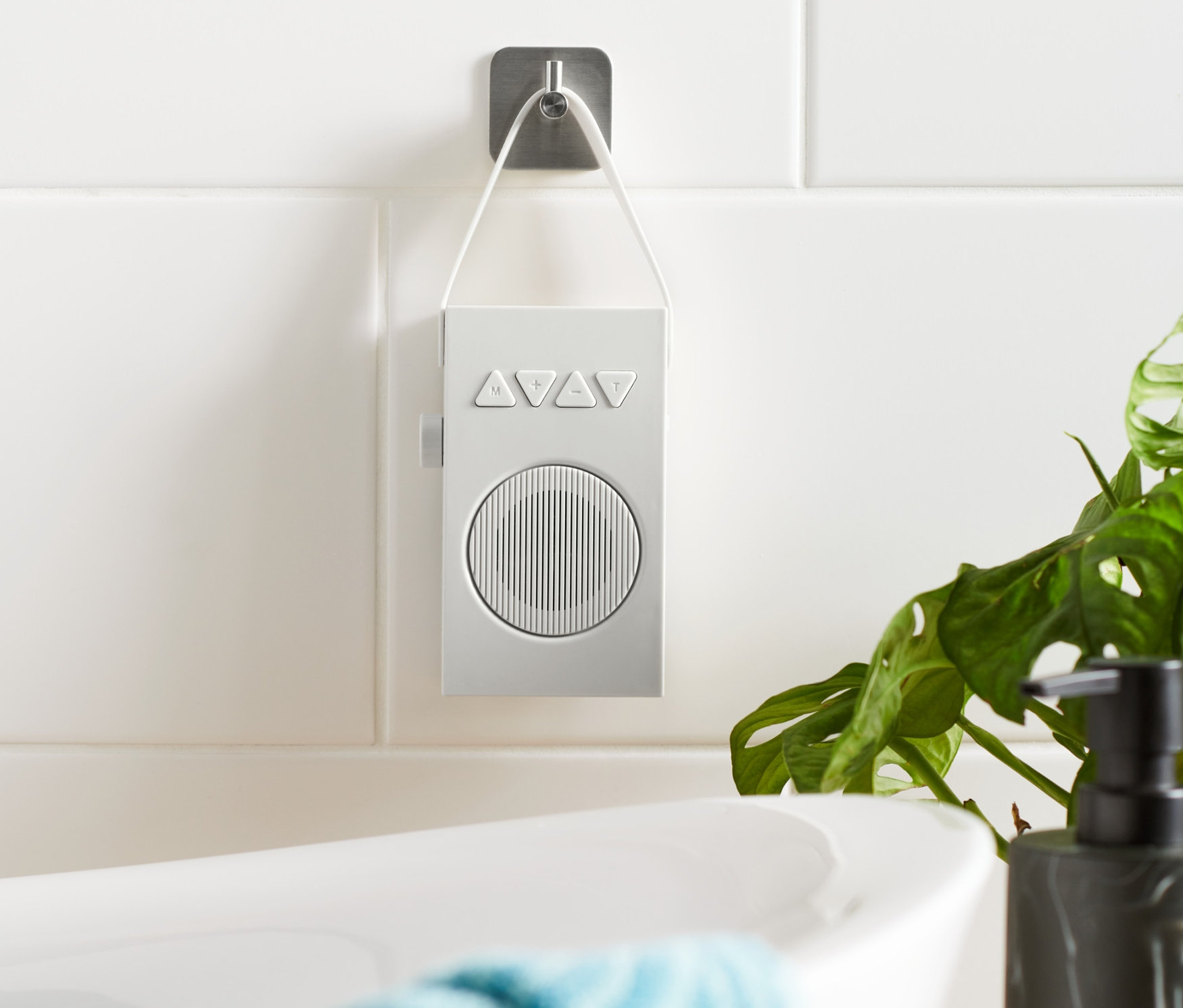 Beyaz bir banyo radyosu, küvetin yanındaki fayanslı duvara asılı duruyor.