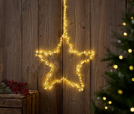 Sarı bir ışıklı yıldız, bir Noel ağacının ve kırmızı meyvelerle dolu bir ahşap kutunun yanında ahşap bir duvara asılıdır.