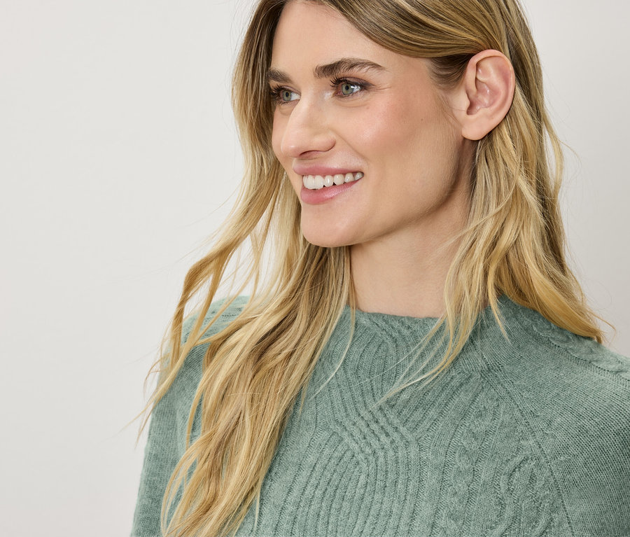 Yeşil bir kazak içinde sarı saçlı, gülümseyen bir kadının profil görüntüsü.