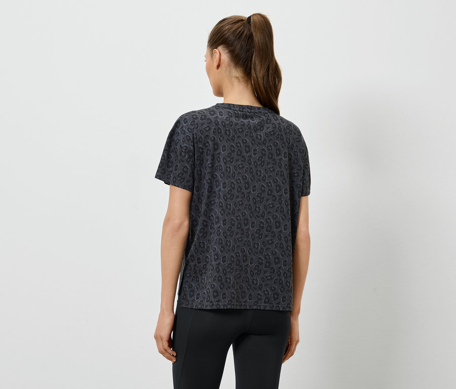 Atkuyruklu kadın desenli, koyu renk bir tişört ve tayt giyiyor, arkadan görünüm.