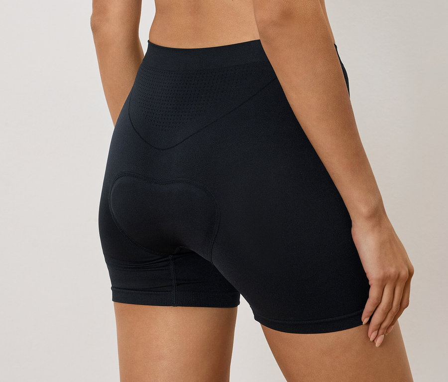 Kadın arkadan görünüşüyle siyah, kalça dolgulu bisikletçi şortu giyiyor.