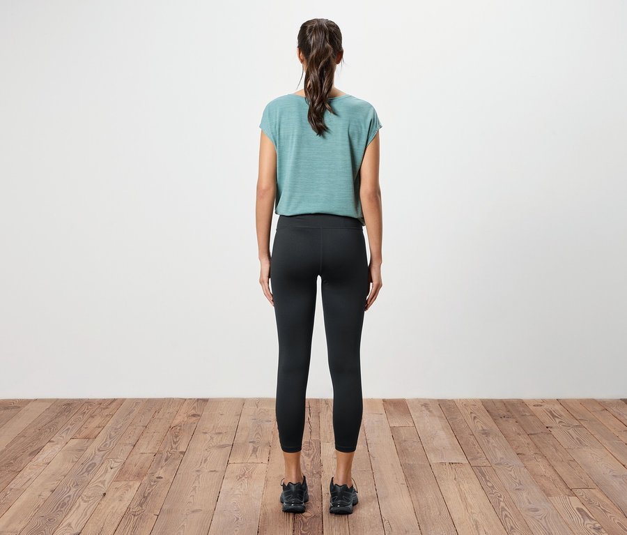 Atkuyruğu olan, deniz mavisi bir üst, siyah tayt ve tahta zeminde siyah spor ayakkabılar giyen bir kadının arka görünümü.