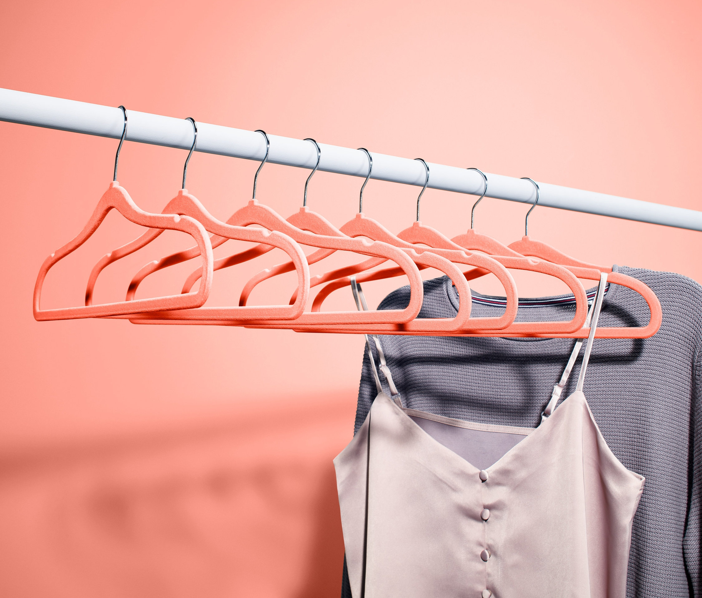 Beyaz bir çubuğa asılmış sekiz adet kıyafet askısı. Bir askıda gri bir kazak ve bir atlet asılı duruyor.