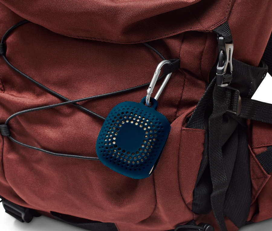 Kahverengi sırt çantası ve üzerinde asılı duran, içinde outdoor el havlusu olan mavi renkli bir kılıf bulunan bir karabina.