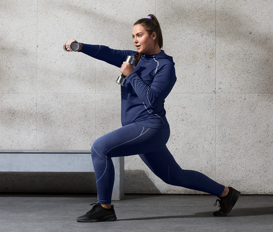 Kadın dambıllarla hamle yapıyor, Kapüşonlu Dikişsiz Fonksiyonel Üst ve Seamless Spor Taytı giyiyor.