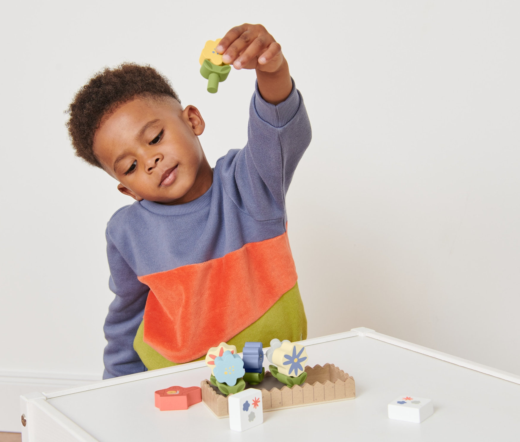 Oğlan tahta oyuncak çiçeklikle oynuyor.