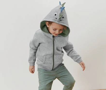 Dinozor aplikeli gri kapüşonlu çocuk sweatshirt'ü giyen bir çocuk ahşap bir tabure üzerinde duruyor.