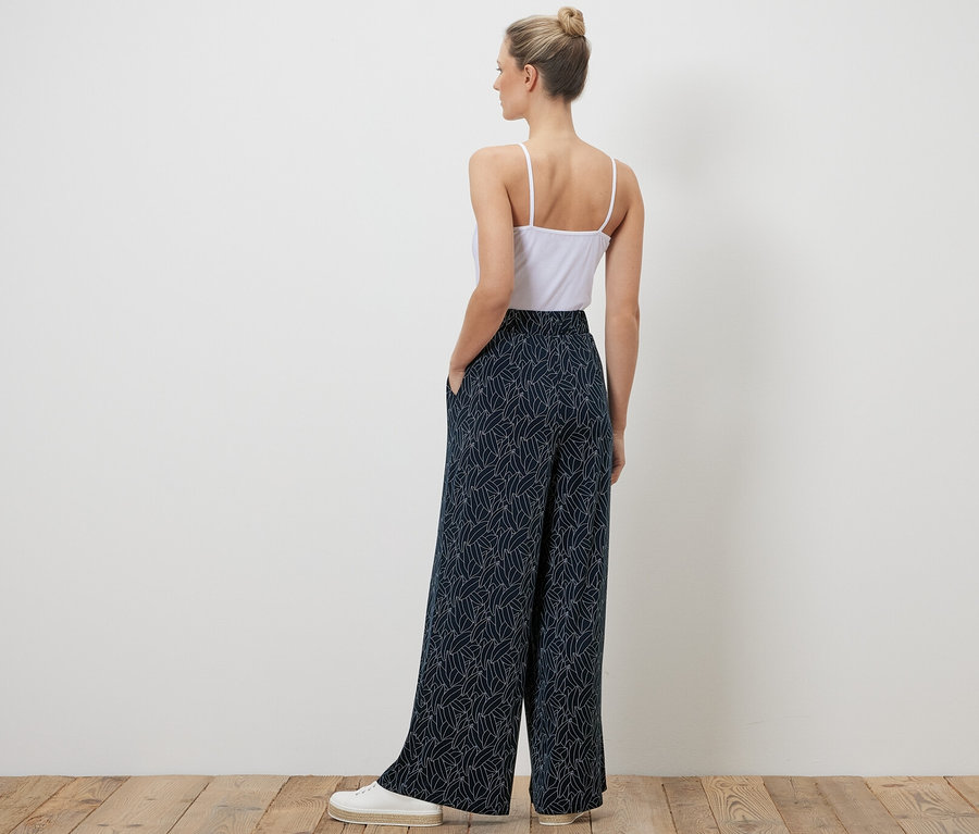 Kadın kameraya arkası dönük duruyor, üzerinde lacivert-krem beyaz baskılı palazzo pantolon var.