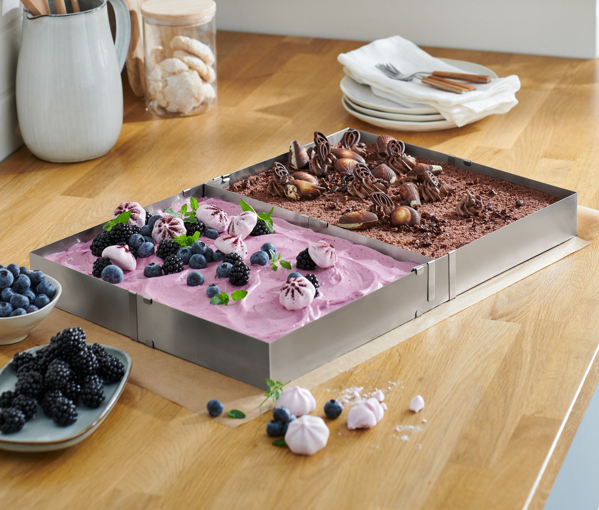 Ahşap bir tezgah üzerinde meyveli ve çikolatalı kek bulunan iki adet paslanmaz çelik fırın çerçevesi.