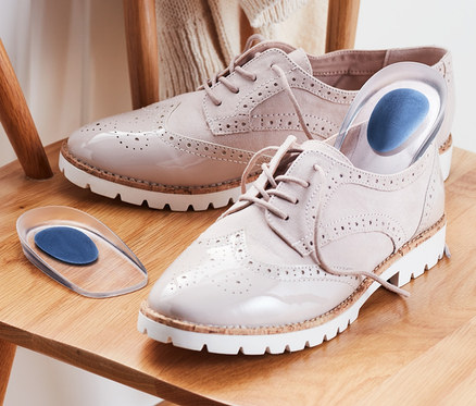 Ahşap bir sandalyede rugan ayakkabılar ve 1 Çift Topuk Desteği bulunmaktadır.