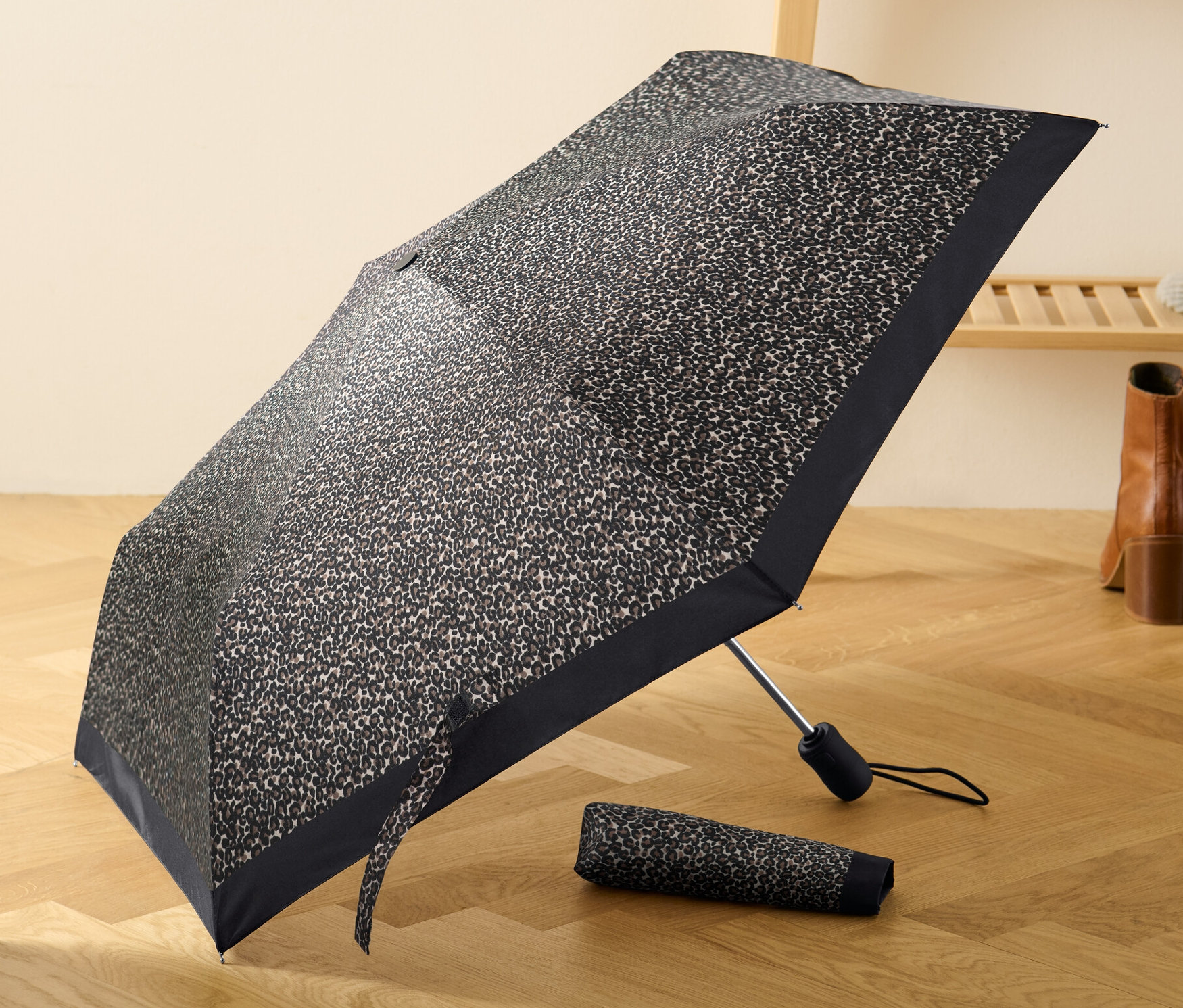 Leopar desenli açık otomatik cep şemsiyesi, katlanmış bir şemsiyenin yanında ahşap bir zeminde duruyor.