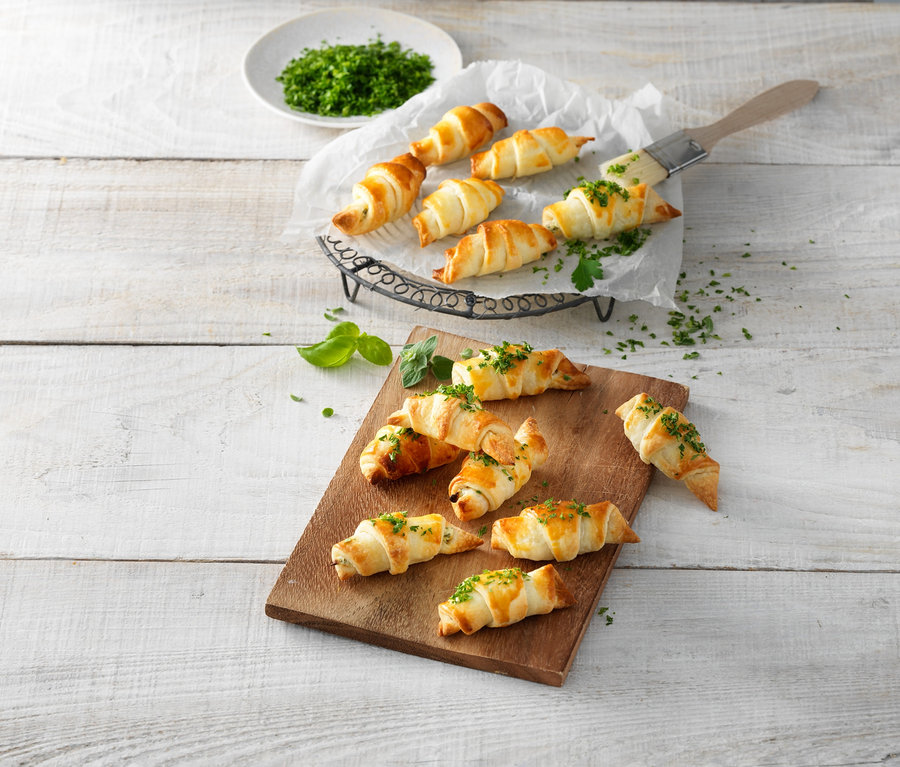 Ahşap kesme tahtası ve tel stand üzerinde otlarla serpilmiş kruvasanlar. Kruvasan Rulosu.