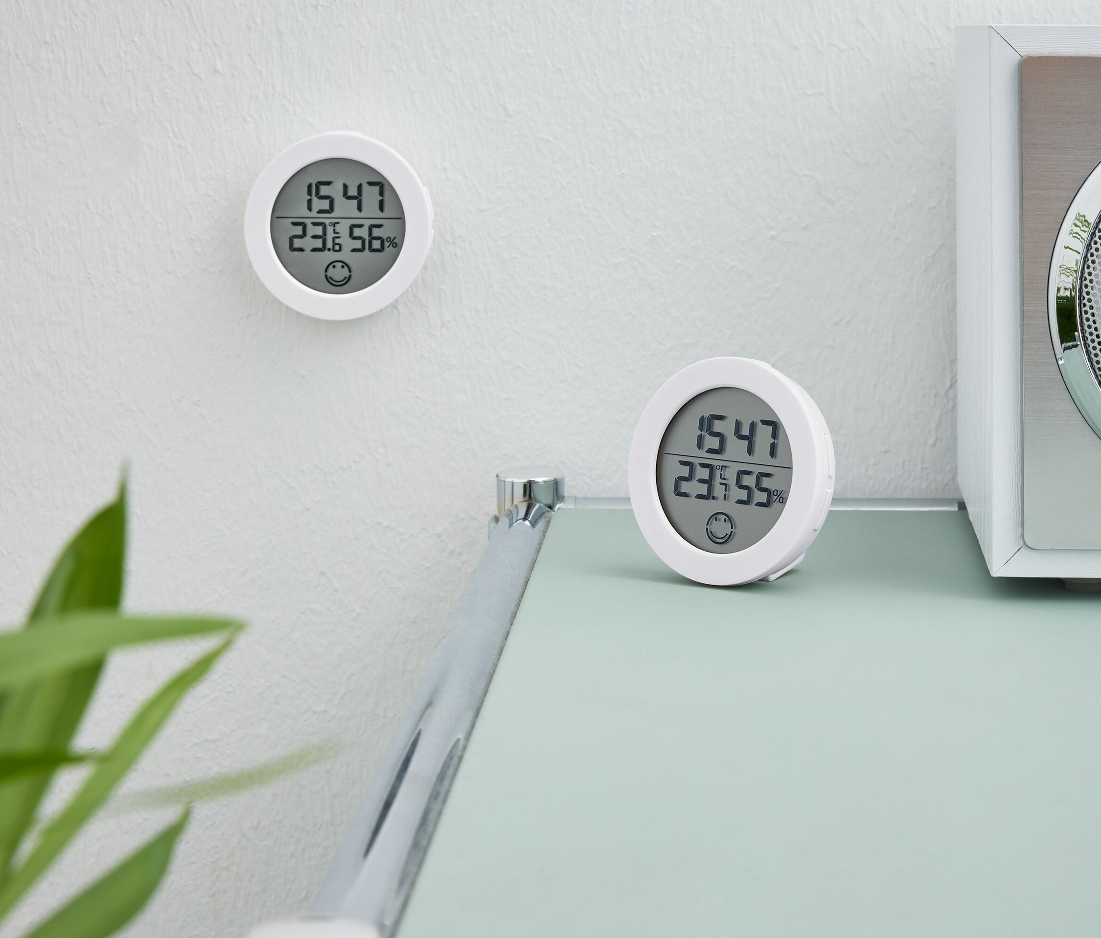 İki beyaz dijital saat. Bir saat duvarda. İkinci saat beyaz bir radyonun yanında bir masanın üzerinde duruyor.