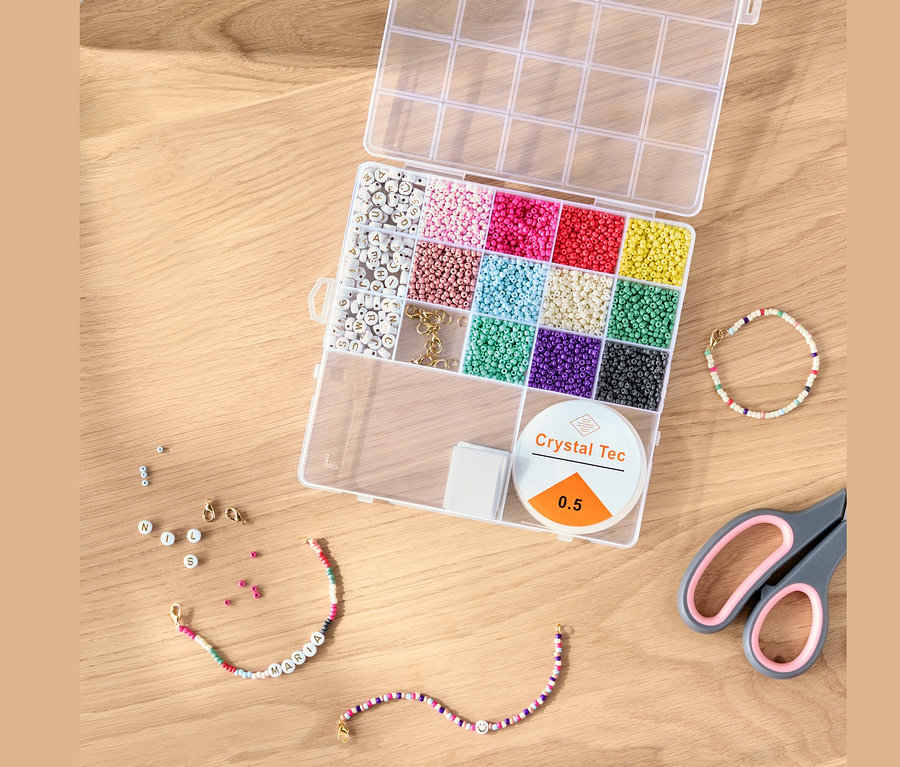 Ahşap bir masa üzerinde renkli boncuklar, ip ve makas bulunan açık bir DIY boncuk seti.