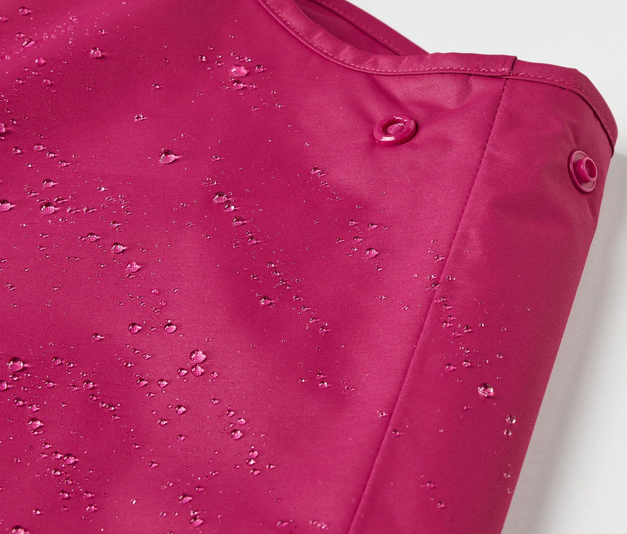 Su damlaları olan böğürtlen rengi çocuk termal yağmur pantolonunun detayı.